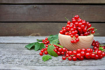  Czerwone porzeczki w drewnianej miseczce na tle desek