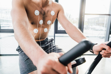 cropped view of sportsman with electrodes training on elliptical during endurance test in sports center