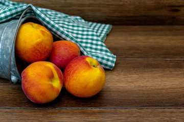 Peaches in a bucket with green picnic tabletop over wooden background with copy space 
