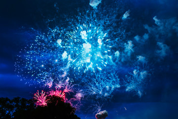 Inexpensive fireworks over blue sky, red, green, blue and white with colour sparks. Selective focus. Bright and shiny. Celebration concept.