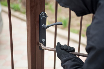 Burglar trying to break the gate with a crowbar. Thief breaking lock to open the gate