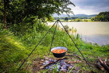 Cooking outdoor on a fire in a pot. Preparing  goulash in a nature by the lake.