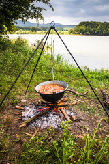 Cooking outdoor on a fire in a pot. Preparing  goulash in a nature by the lake.
