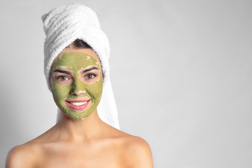 Young woman with clay mask on her face against light background, space for text. Skin care