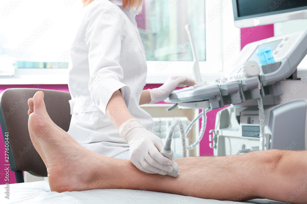 Wall mural Doctor conducting ultrasound examination of patient's leg in clinic, closeup