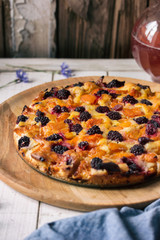 Homemade cake with blackberries, apricots, gooseberries. Cake stands on a white wooden table. Next to the decanter with a pink compote
