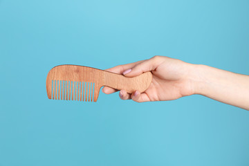 Woman holding wooden hair comb against blue background, closeup