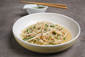 Plate of noodles with broth and herb on grey background, closeup