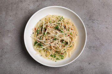 Plate of noodles with broth and herb on grey background, top view
