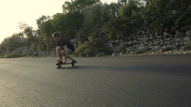 Slow motion video of a young male adult turning on a skateboard in a low position like surfing. Camera movement follows actor.