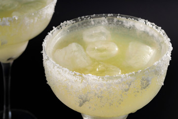 Tropical cocktail, Mexican drink and cinco de mayo party concept theme with close up on two glasses of margarita on the rocks with salted rims isolated on black background