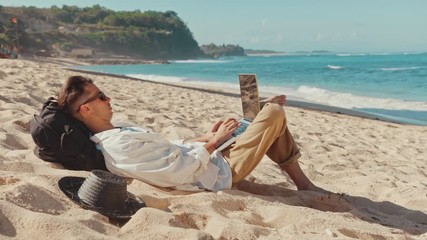 Freelancer Man Working Using Laptop Sitting On The Beach. Freelancer working on new startup project using laptop computer and wireless connection. Freelance Summer Travel Remote job concept - Powered by Adobe