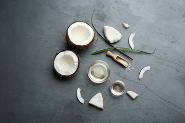 Bowls of natural organic oil and coconuts on grey stone background, flat lay
