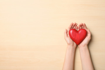 Woman holding heart on wooden background, top view with space for text. Donation concept