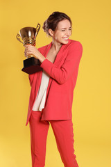 Portrait of happy young businesswoman with gold trophy cup on yellow background