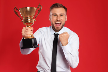 Portrait of happy young businessman with gold trophy cup on red background