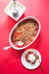 Crunchy strawberries and rhubarb crumble with vanilla ice cream,top view, red background