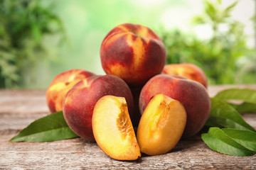 Fresh juicy peaches and leaves on wooden table against green blurred background