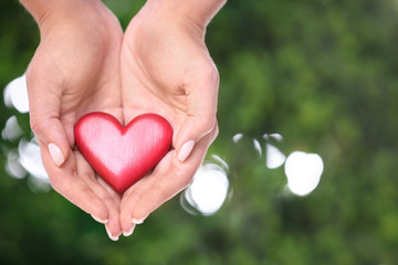 Young woman holding red heart on blurred green background, closeup with space for text. Donation...