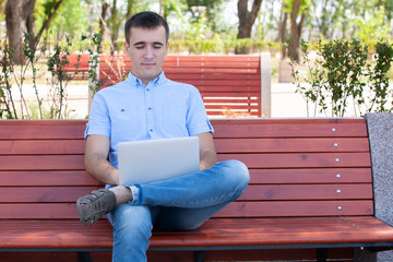 Young man with laptop sitting on a wooden bench