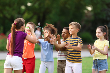 Cute little children playing with soap bubbles in park