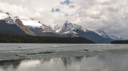 Fototapeta na wymiar Cloudy Rocky mountains in British Columbia reflecting in the icy water
