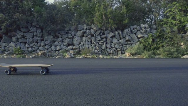 Slow motion video of an unrecognizable young skateboarder jumping on a moving skateboard. Still shot, actor moving from left to right.