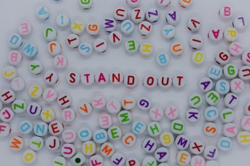 Stand Out, spelt out in red letters, surrounded by a sea of random letters, on a white background. ...