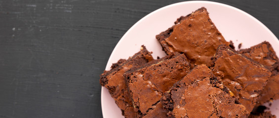 Freshly baked chocolate brownies on a pink plate on a black surface, top view. From above,...