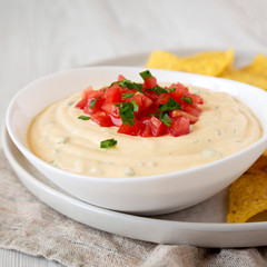 Homemade cheesy dip in a bowl, yellow tortilla chips, low angle view. Close-up.