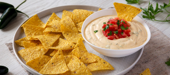 Homemade cheesy dip with yellow tortilla chips on a white wooden background, low angle view. Close-up.