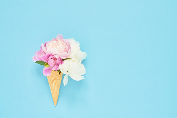 Peonies flowers bouquet in waffle ice cream cone on light blue background. Summer concept. Copy space, top view
