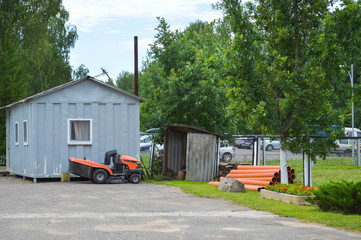 A large professional agricultural lawn mower, a lawn mowing tractor with grass, stands near the tool shed
