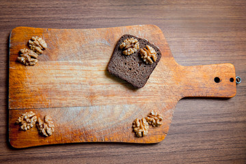 A piece of black rye bread with walnuts on a wooden chopping Board.