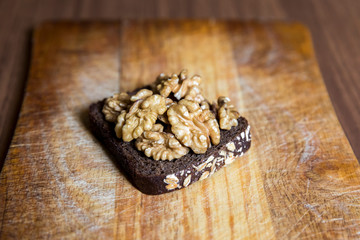 A piece of black rye bread with walnuts on a wooden chopping Board.