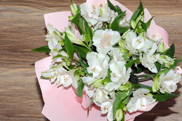 Bouquet of alstroemeria flowers in pink decorative paper close-up on wooden background.