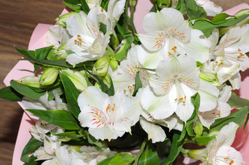 Bouquet of alstroemeria flowers in pink decorative paper close-up on wooden background.