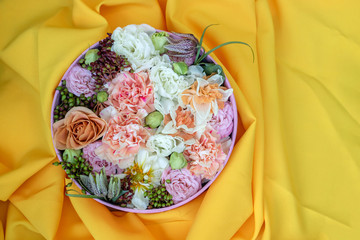 Bouquet of roses, daffodils, eustoma and other flowers on a yellow background. The idea of a floral arrangement in a round box.