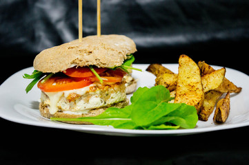  Salmon burger with rustic potatoes and rucula leaves.
