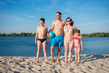 A happy family on the beach.  People having fun on summer holidays.  Father, mother and children against the blue river and sky.