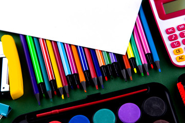 School office supplies stationery on a green background desk with white paper above copy space. Back to school concept.