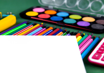 School office supplies stationery on a green background desk with white paper above copy space. Back to school concept.