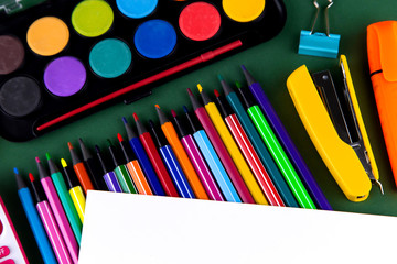 School office supplies stationery on a green background desk with white paper above copy space. Back to school concept.