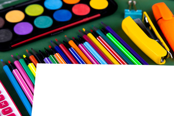 School office supplies stationery on a green background desk with white paper above copy space. Back to school concept.