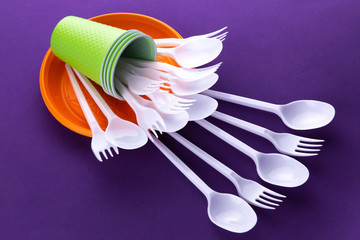 Bright orange and green set of disposable plastic tableware on purple background. Ecology problem. No plastic concept.