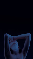 Man In the moonlight looks into the sky closing his eyes with hands. Black background. A man...