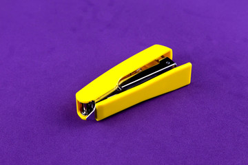 School stationery yellow stapler isolated on purple background close up