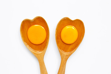 Egg yolk and white on  wooden spoon heart shape on white background.