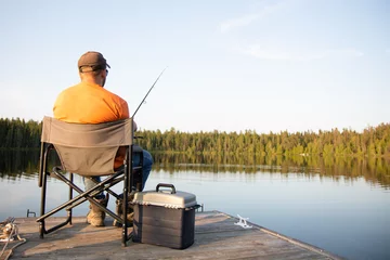Gordijnen A man fishing on a lake on a wooden dock in Ontario Canada © Ashley