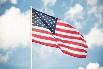 An American flag fluttering in the wind against a blue sky with clouds.